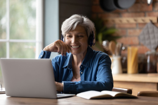 woman sitting at table wearing headphones and smiling at a laptop computer screen