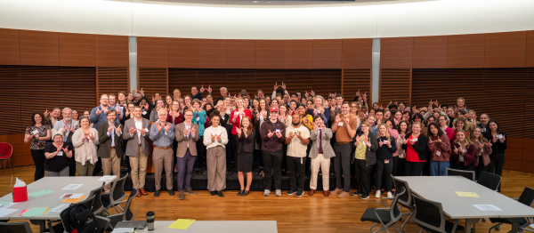 The audience of ADRD Research Day 2025 stands together and holds up their hands to make a 'W' shape for UW-Madison