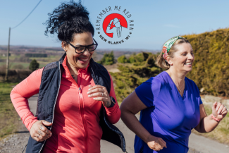 Two people jogging on a rural road wearing athletic clothing, with the ‘Remember Me Red Run – New Glarus, WI’ event logo displayed above them.