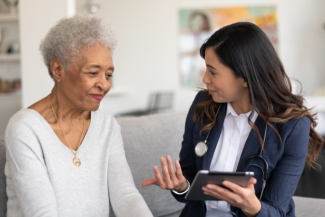 A healthcare professional reviews information on a tablet with an older adult during an in‑home consultation.
