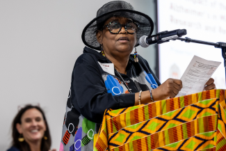 Dr. Fabu Carter speaking at a podium with Dr. Carey Gleason looking on smiling