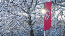 Snowy day with sunshine peeking through the trees, UW crest on a red flag