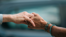 Two hands from different people, one older and one younger, are held together in the center of the photo